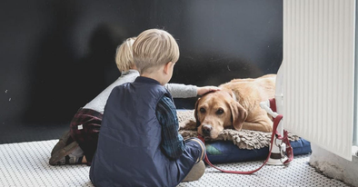 two kids sit petting a dog that's laying down