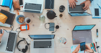 table covered in office supplies and laptops with fingers at work