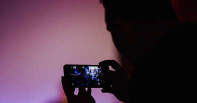 a man filming on his phone against purple background
